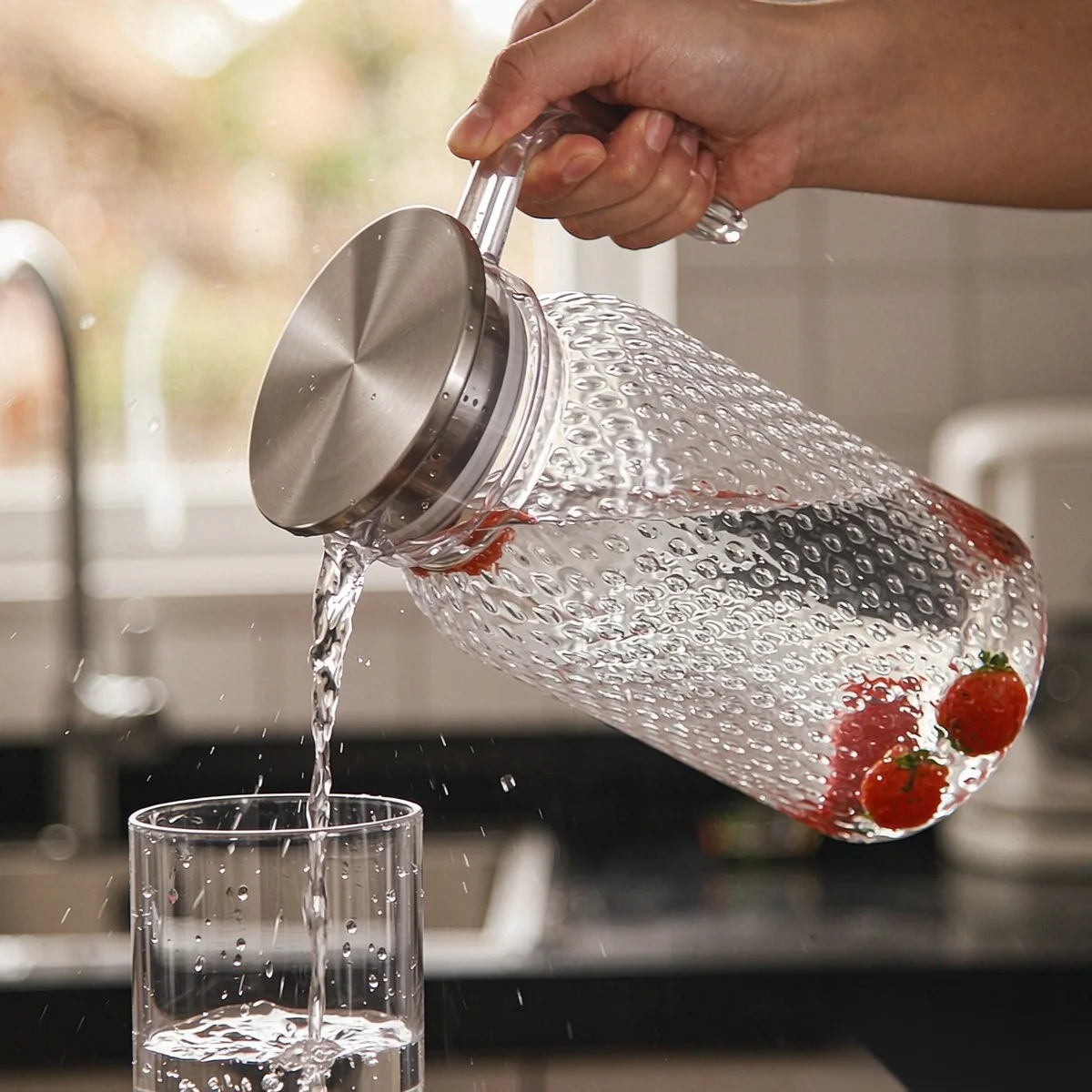 Clear unbreakable polycarbonate water pitcher with a stainless steel handle being poured into a glass on a hotel dining table, wholesale drinkware by Benyang Supplies